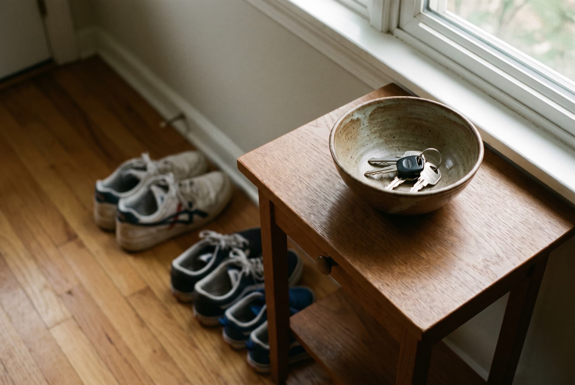 Keys resting in a ceramic bowl by a window, with family shoes lined up near the front door.